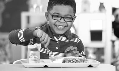 Elementary age black boy child smiling eating school lunch