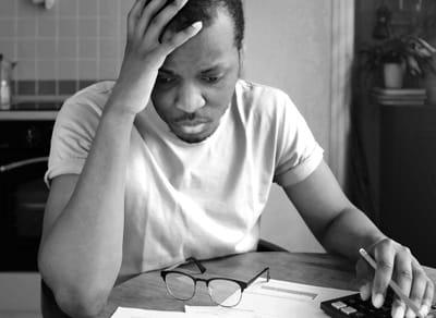 Black man at kitchen table, head in hands, looking at bills and paperwork