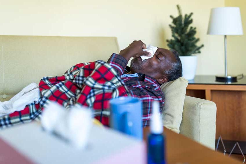Man blowing his nose laying on couch